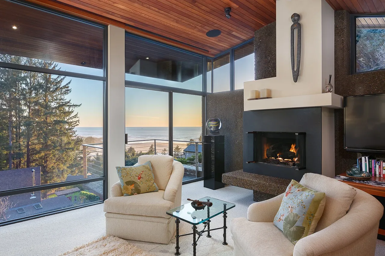Living space features expansive floor-to-ceiling glazing with ocean views and a contemporary fireplace.