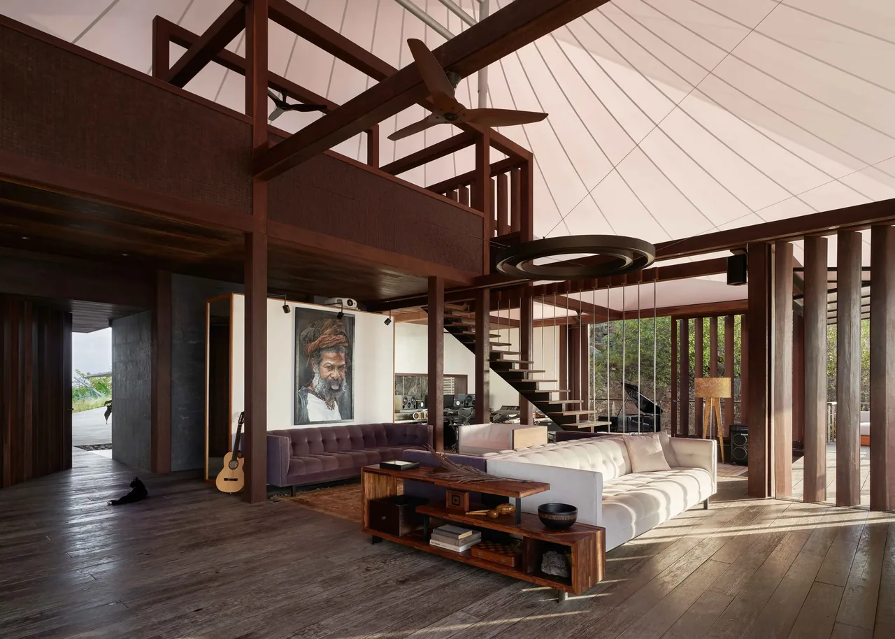 Living area with wood flooring, floating stairs, and ample natural light under a high ceiling.