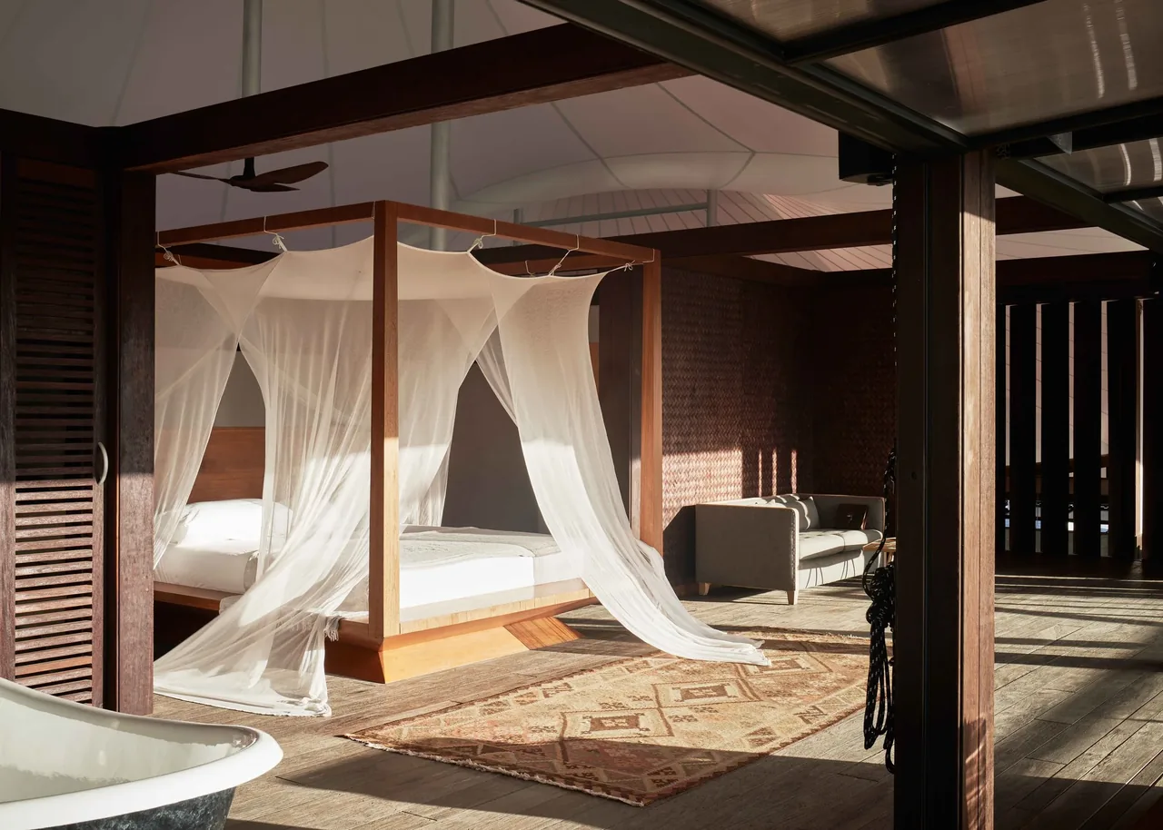 Interior view of a bedroom and sitting area featuring a four-poster bed with sheer fabric and wooden accents