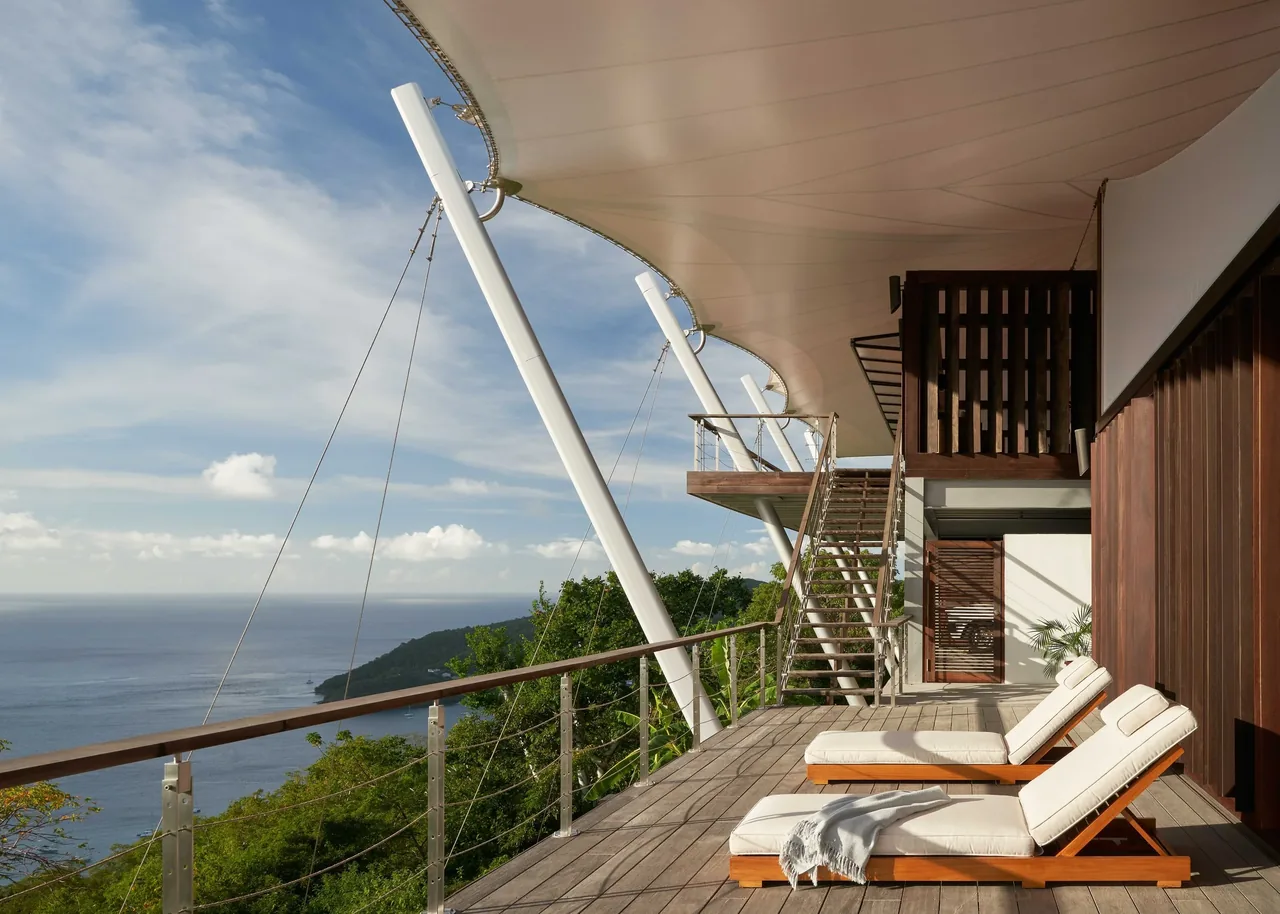 Deck area with sun loungers under a triangular shade sail overlooking a coastal view at SAIL HOUSE, Los Angeles.