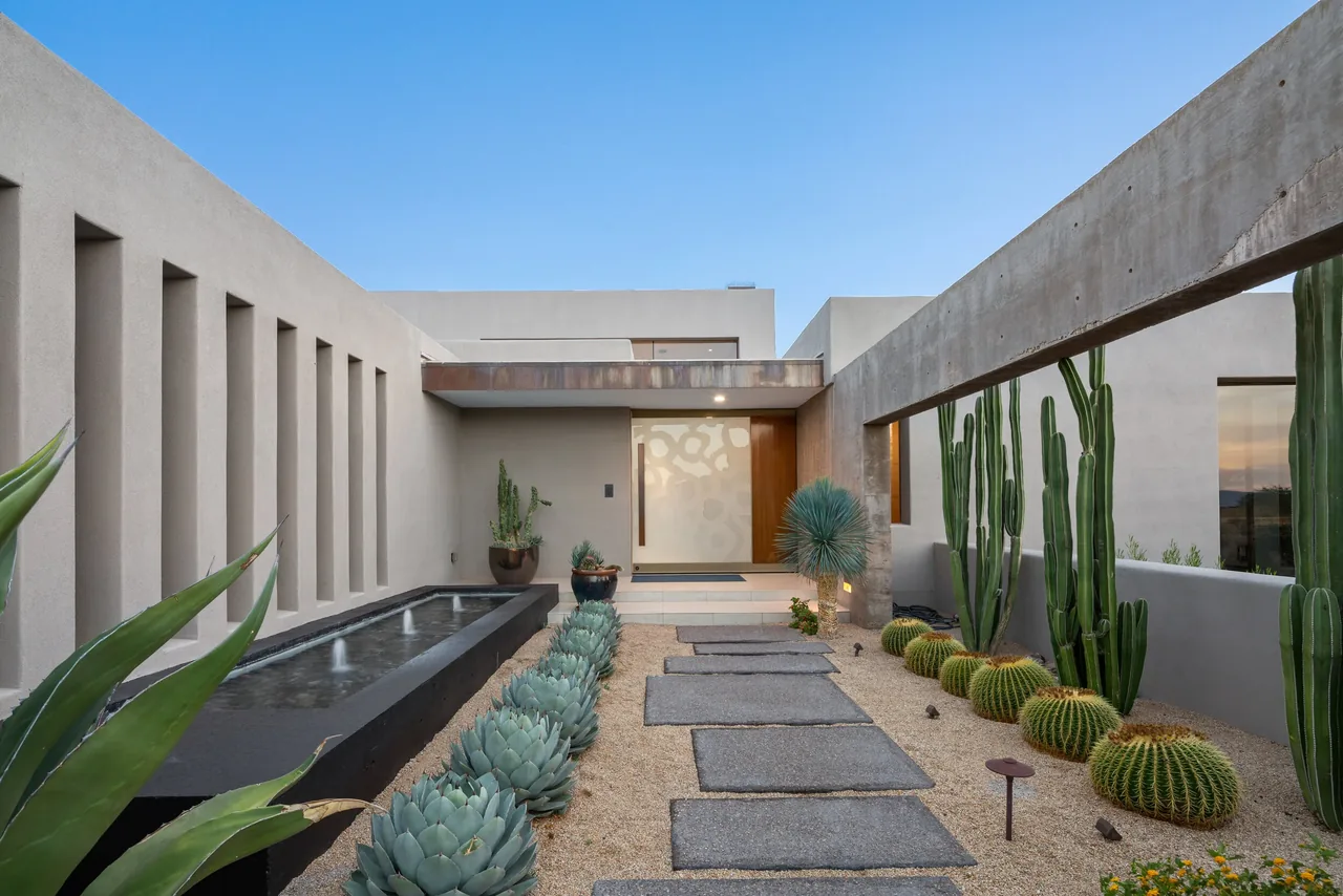 Entry courtyard of the Kim Residence features desert landscaping, a water feature, and a wood-accented modern door in a stucco exterior.