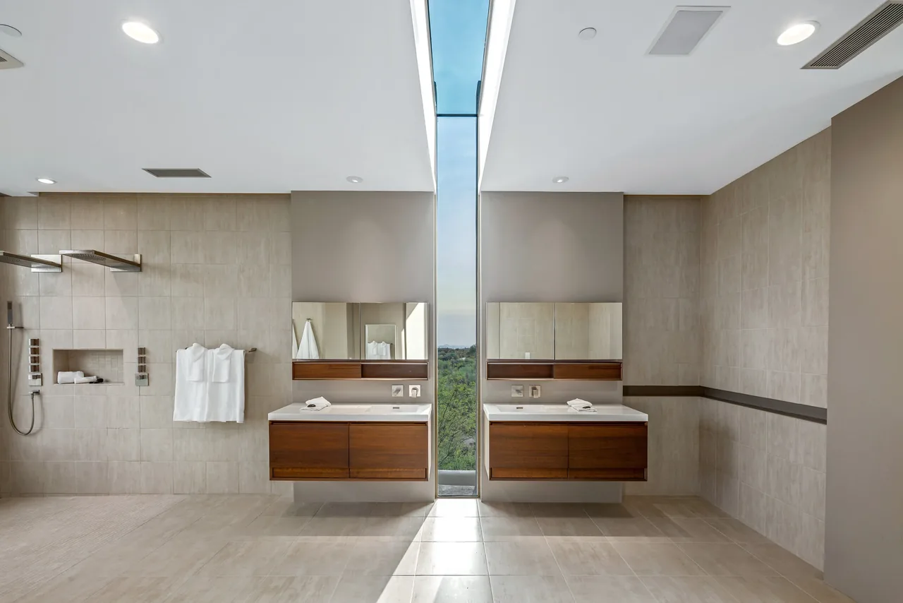 Kim Residence bathroom features dual floating wood vanities and a central vertical window with a desert landscape view.