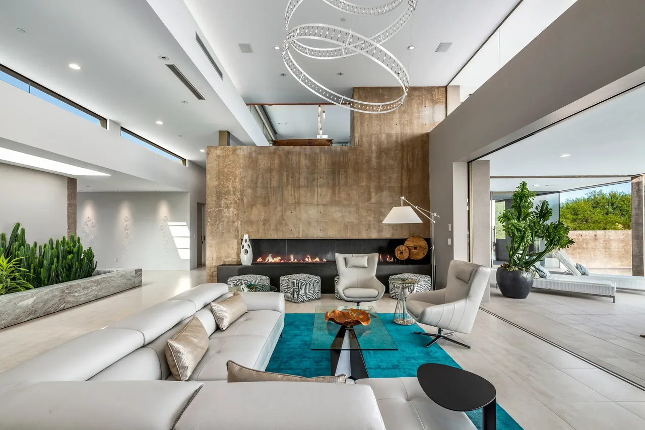 The Kim Residence living room features a concrete fireplace wall and opens to an outdoor living area through sliding glass doors.