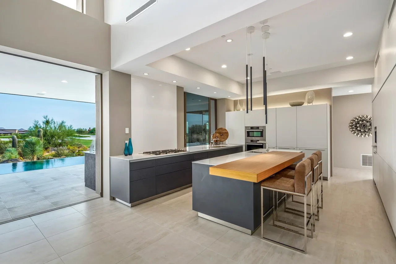 Modern kitchen in the Kim Residence features a wood countertop island and opens to an outdoor patio with a pool and desert plants.