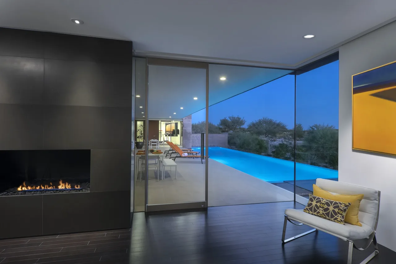 Kim Residence living room features a modern fireplace and large glass sliding doors opening to a pool and desert landscape views.