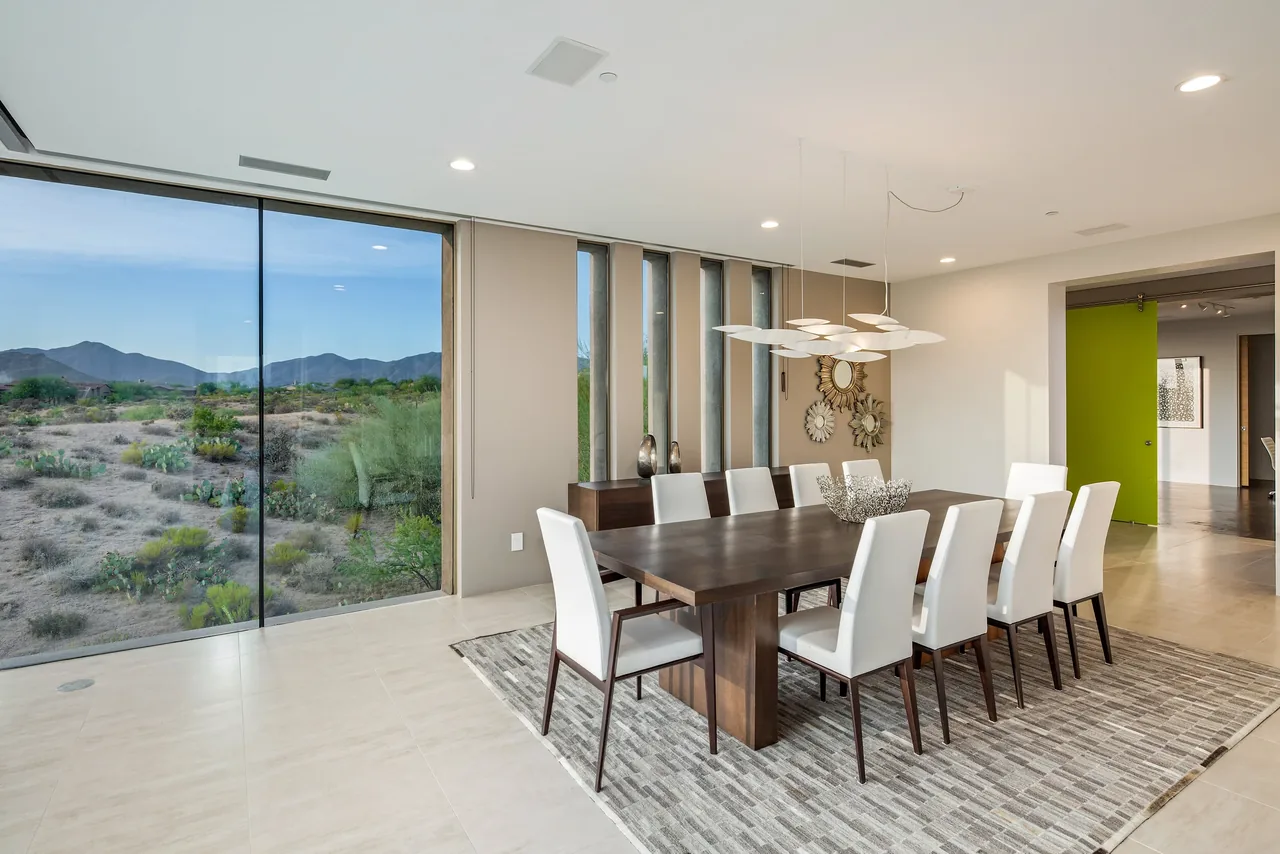 Kim Residence dining room features a large wood table and floor-to-ceiling windows with desert views.