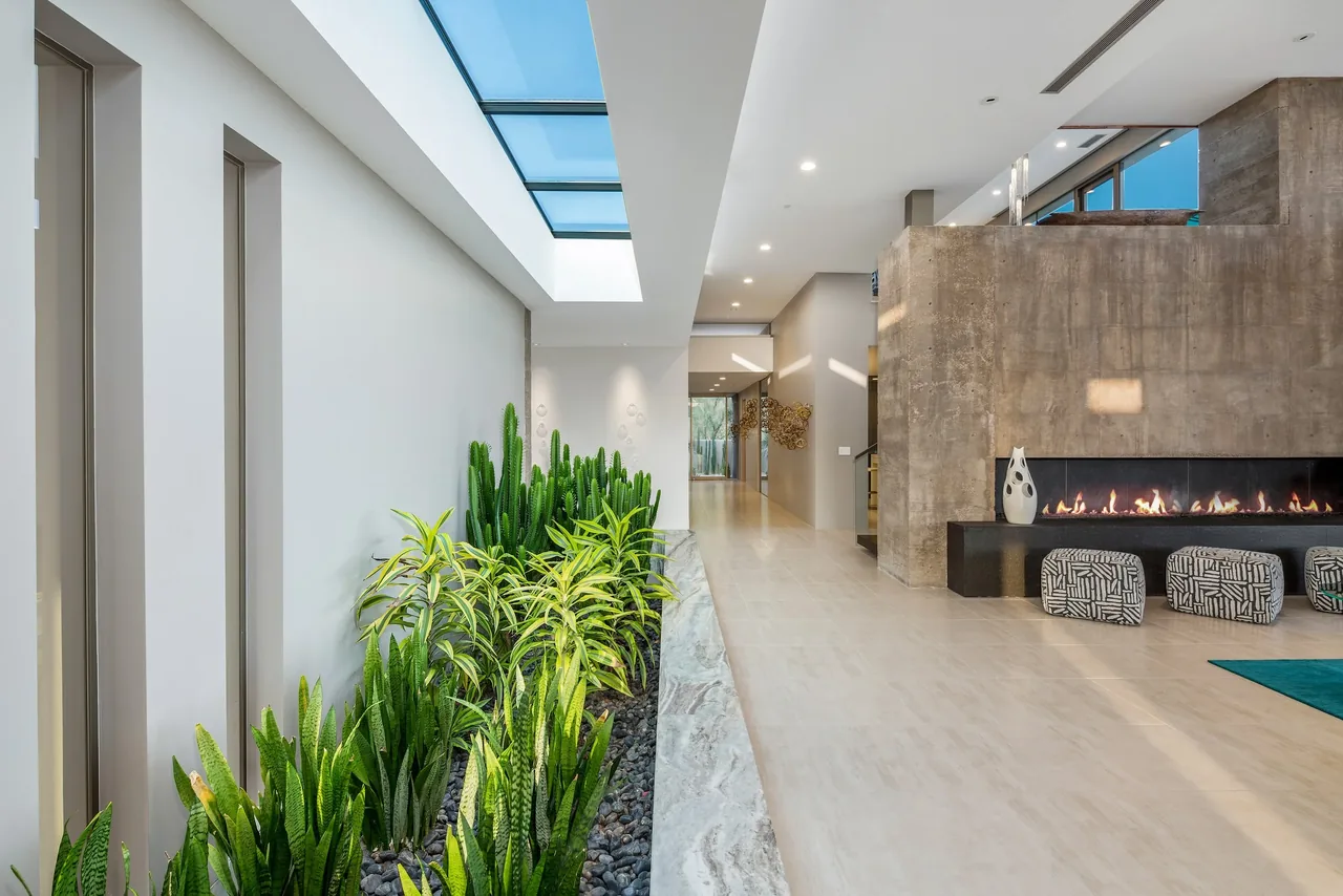 Kim Residence features an indoor garden corridor lit by a skylight, adjacent to a concrete fireplace with seating.