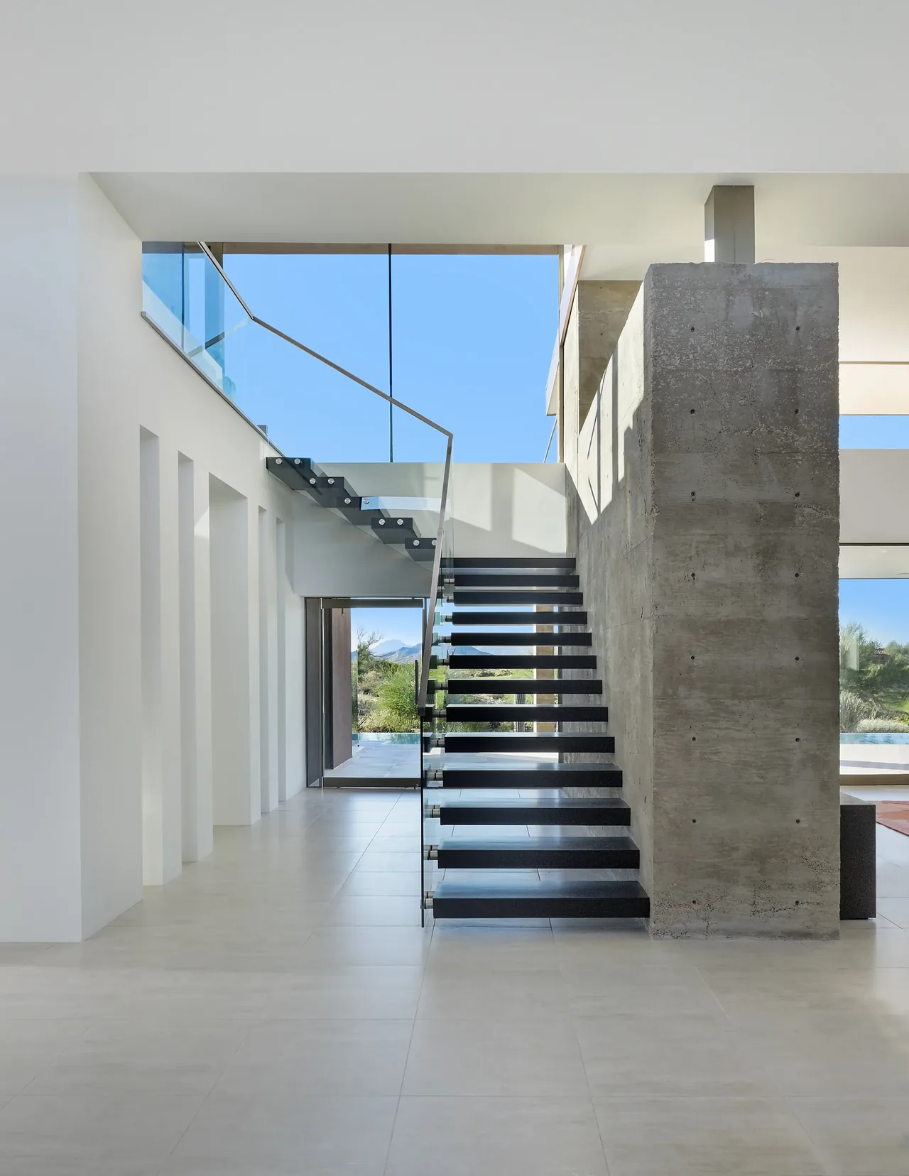 Modern interior stair with floating black steps and a glass railing accentuated by a concrete wall at the Kim Residence.