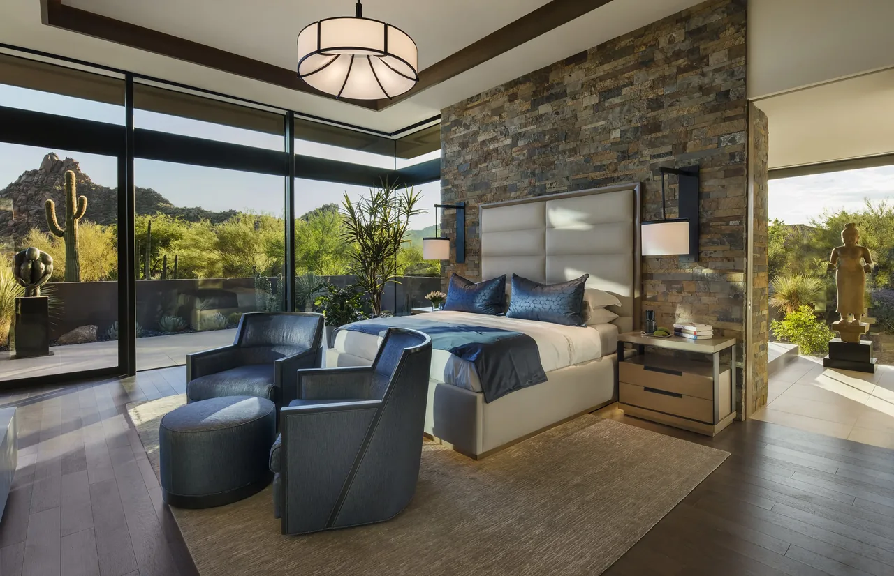 The Silversmith Residence bedroom features a stone accent wall and expansive glazing with desert views.