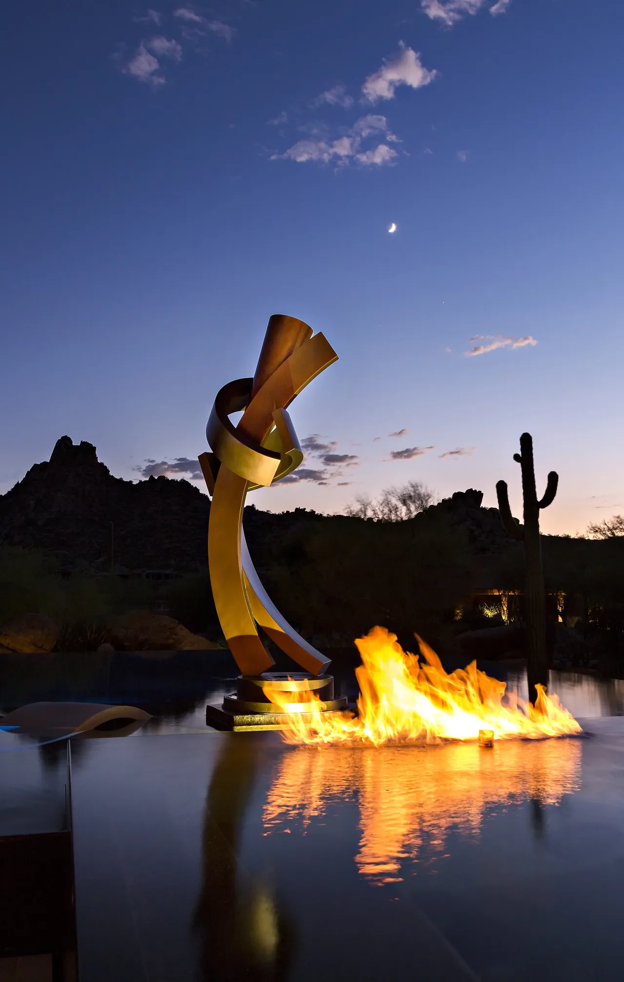 The Silversmith Residence features an abstract metal sculpture beside a linear fire feature in a reflecting pool at dusk.