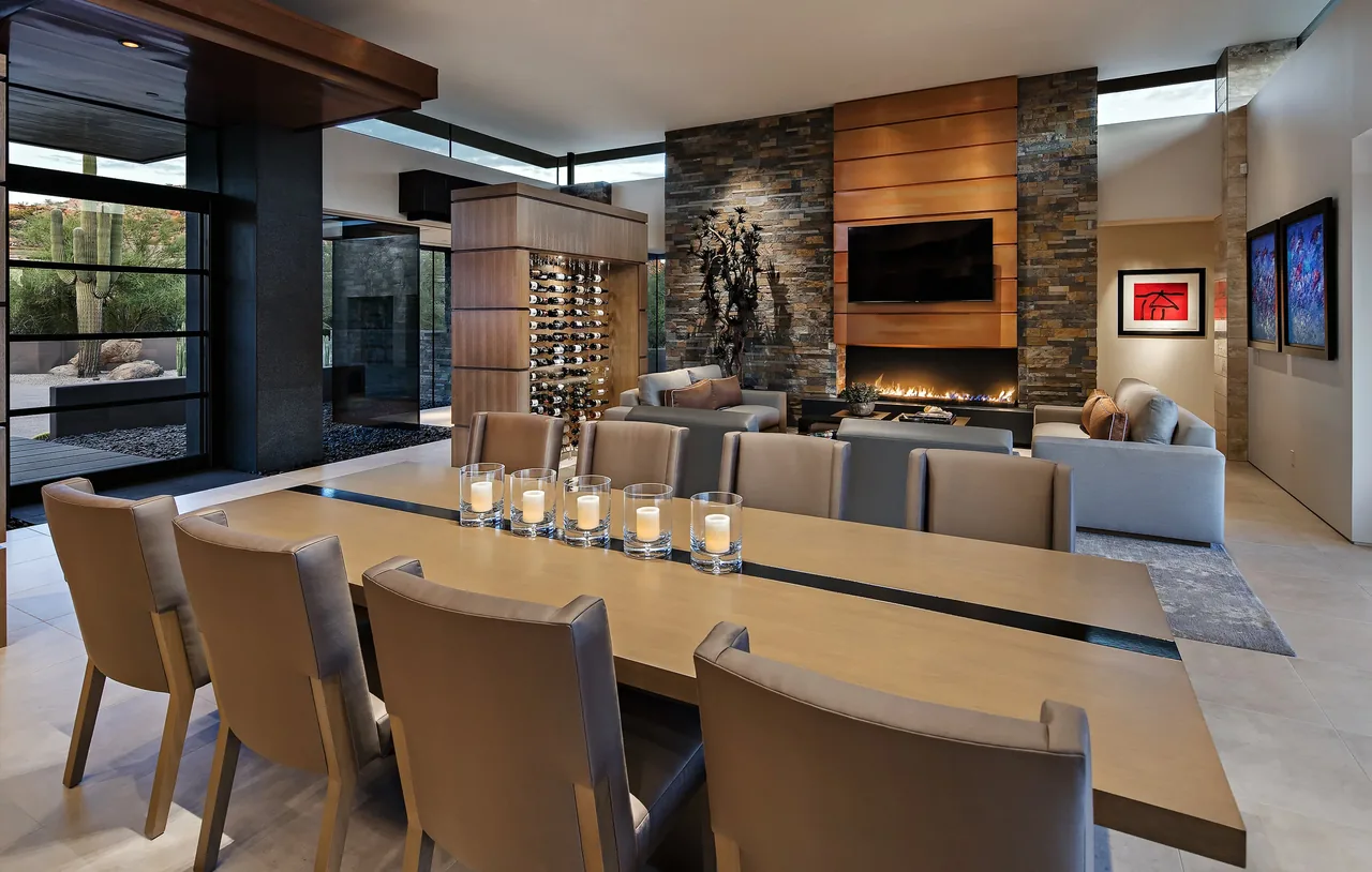 Silversmith Residence living and dining area features a stone fireplace, leather chairs, and floor-to-ceiling windows overlooking a desert landscape.