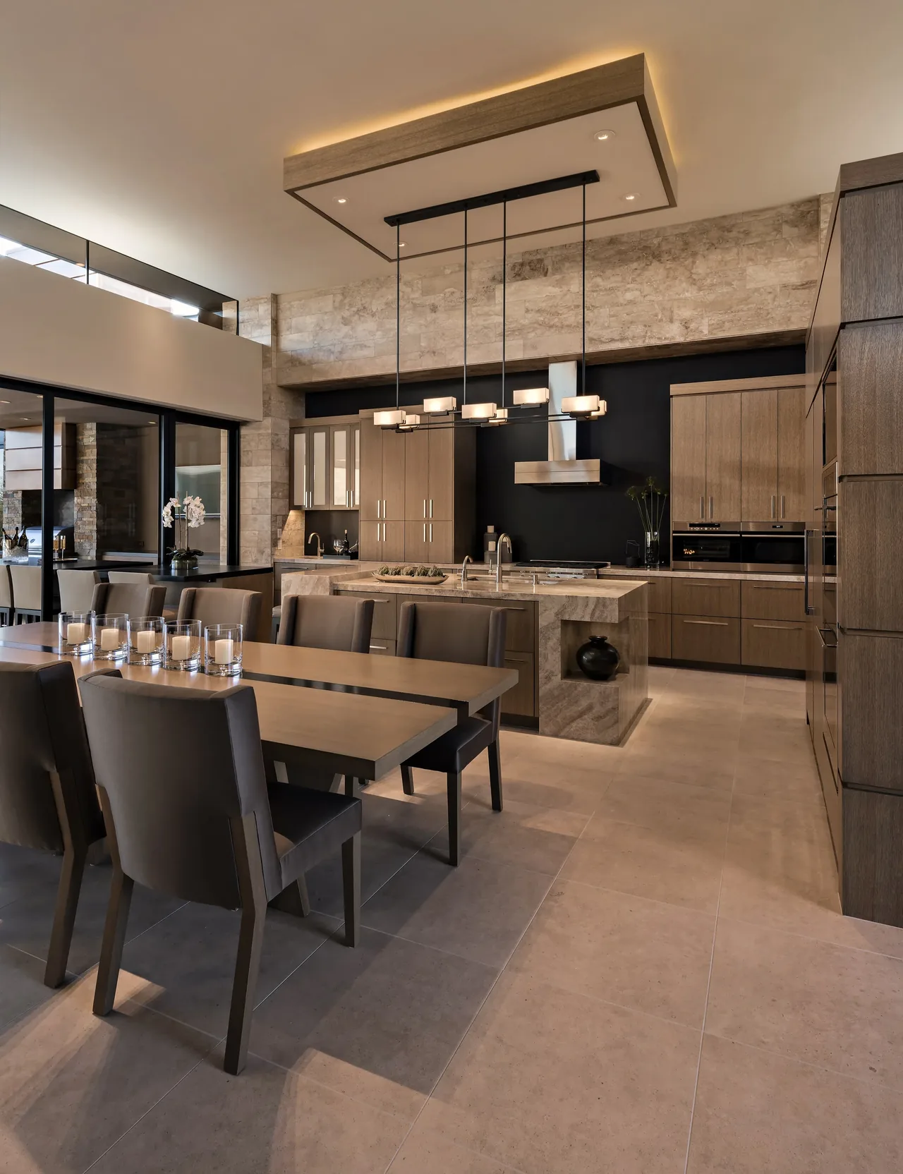 The Silversmith Residence kitchen and dining room showcase stone floors and wood cabinetry with a contemporary lighting fixture.