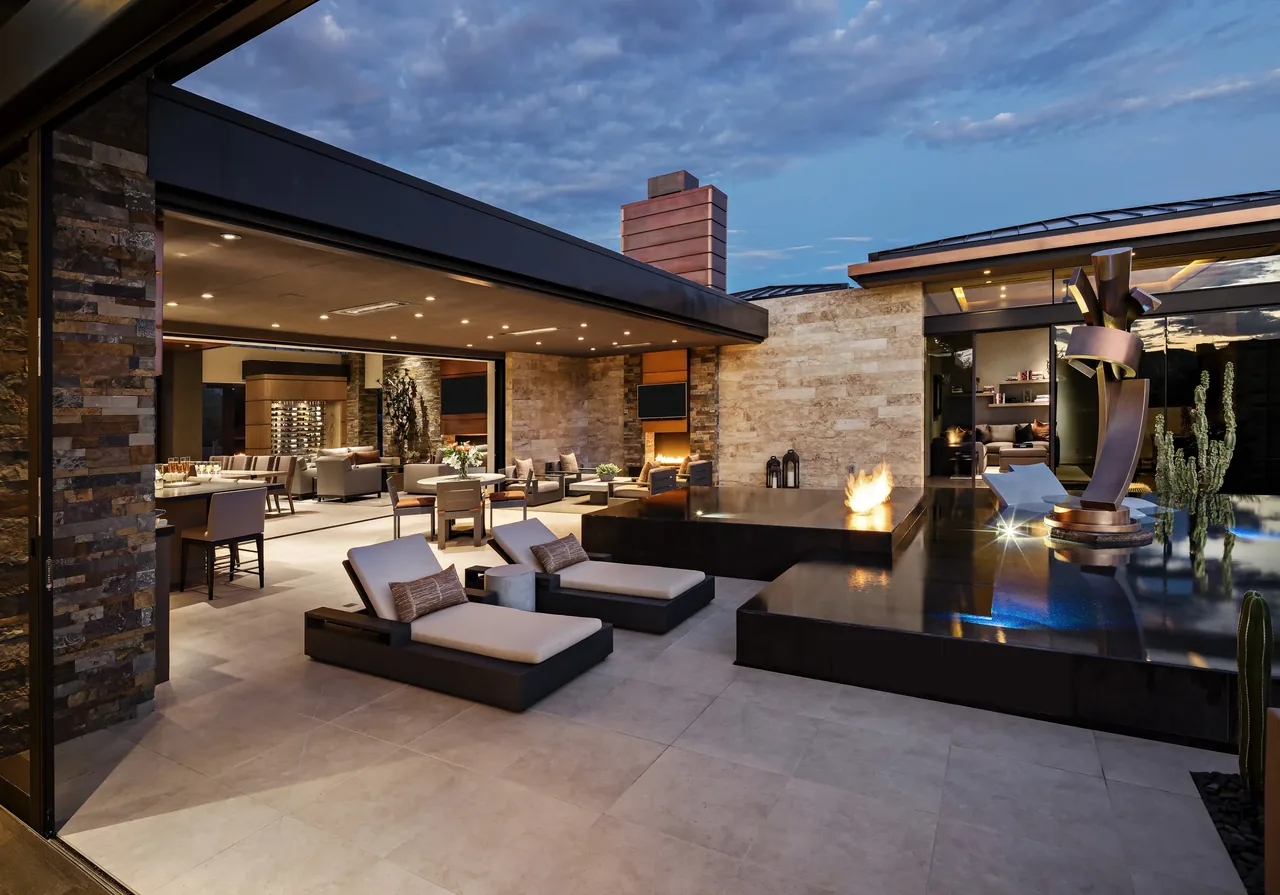 Patio and outdoor living area with chaise lounges, fire feature, and sculptural water element at Silversmith Residence.