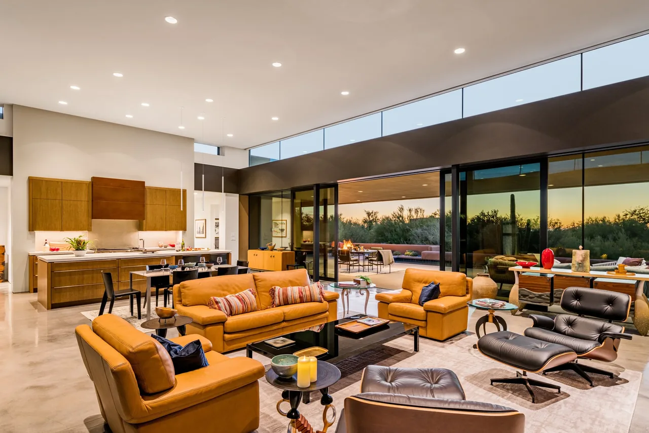 Shea-Naito Residence features an open-concept living and kitchen area with expansive glass walls opening to outdoor living in the evening light.