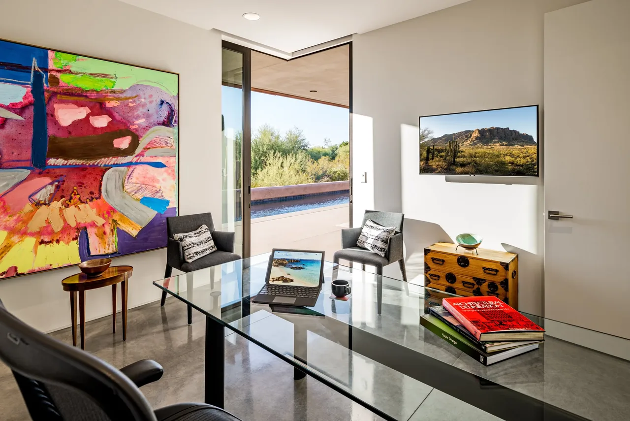 Office space with polished concrete floor, large abstract wall art, and glass desk overlooking desert landscape from Shea-Naito Residence.