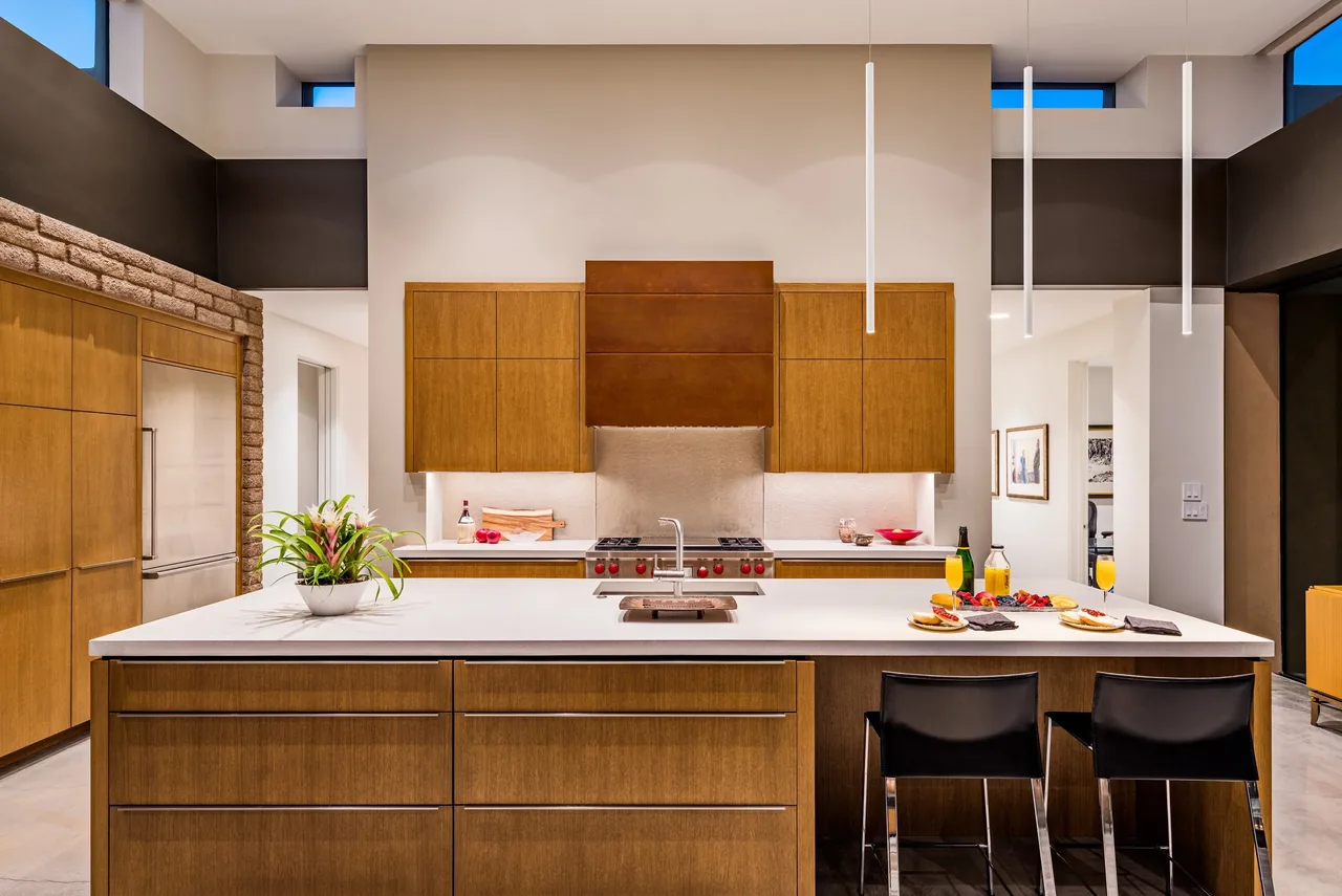 Kitchen at the Shea-Naito Residence features wood cabinets, a white island, and pendant lighting under clerestory windows.