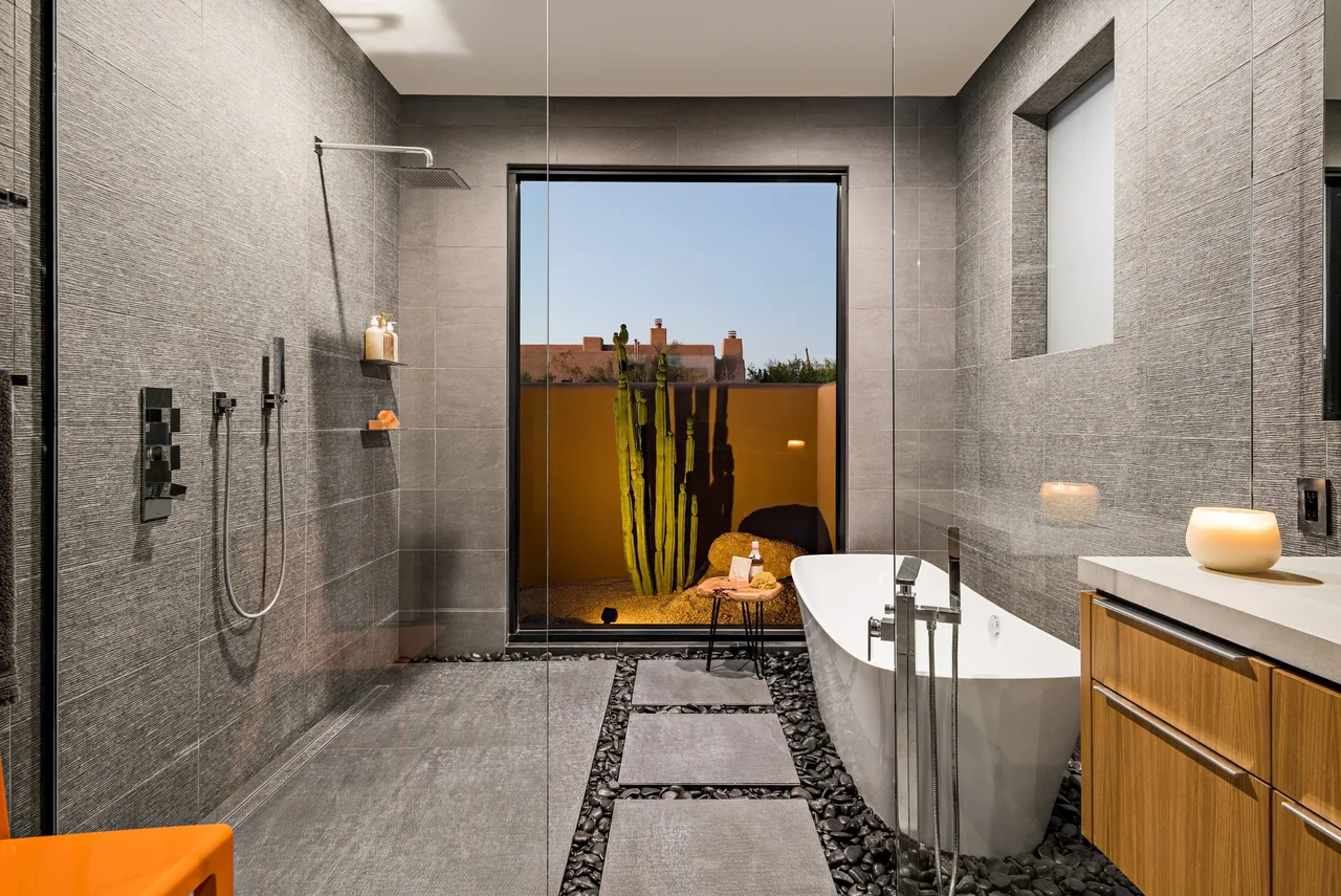 Shea-Naito Residence bathroom features a frameless glass shower, freestanding tub, and a large window with a desert landscape view.