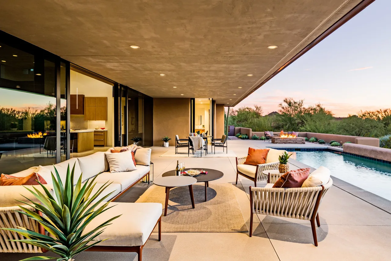 Outdoor living area features wicker seating, a built-in fire pit, and a pool adjacent to sliding glass doors.
