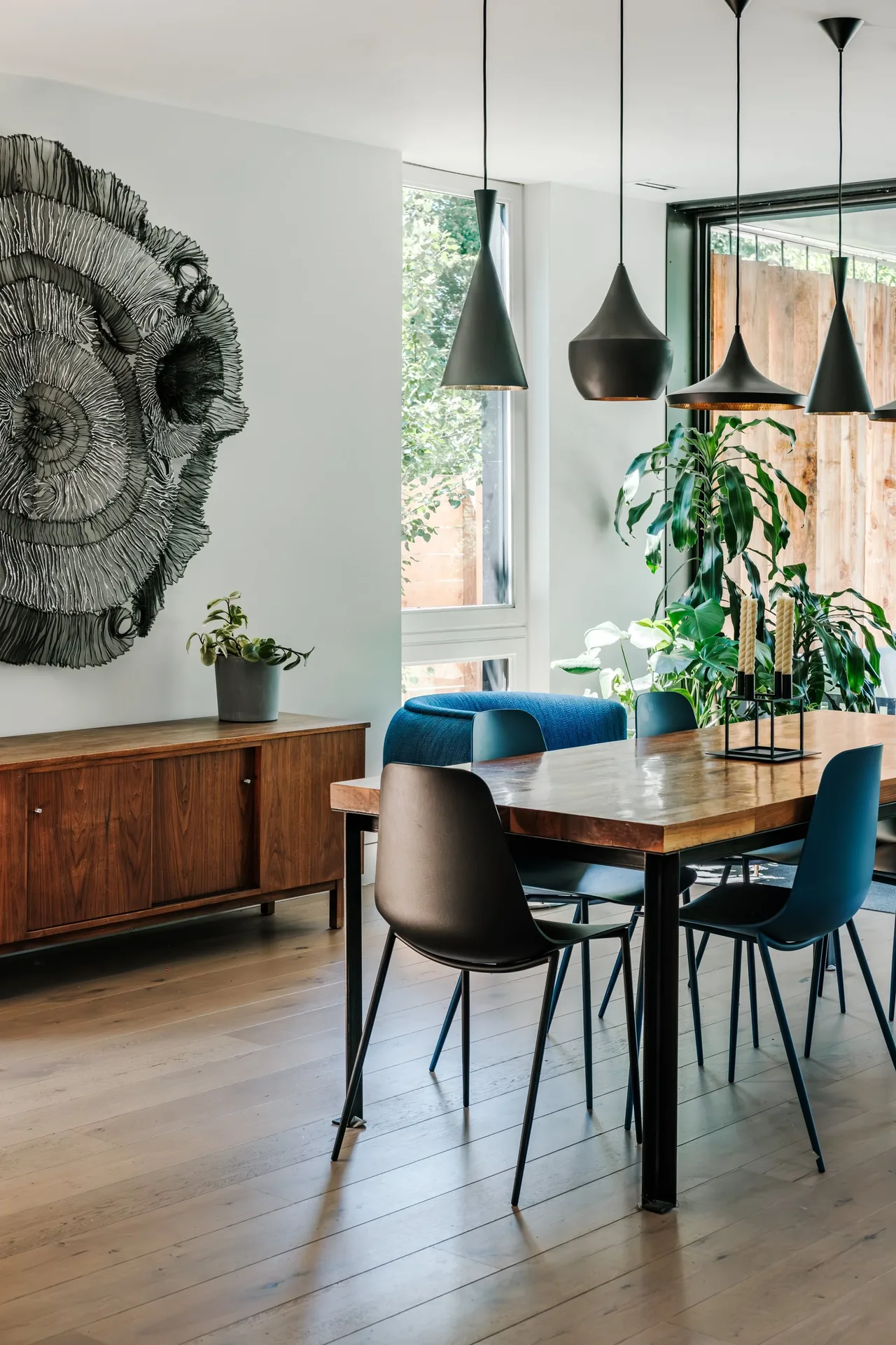 Dining room featuring a wooden table, black chairs, pendant lights, and a wooden sideboard with a modern art piece on the wall.