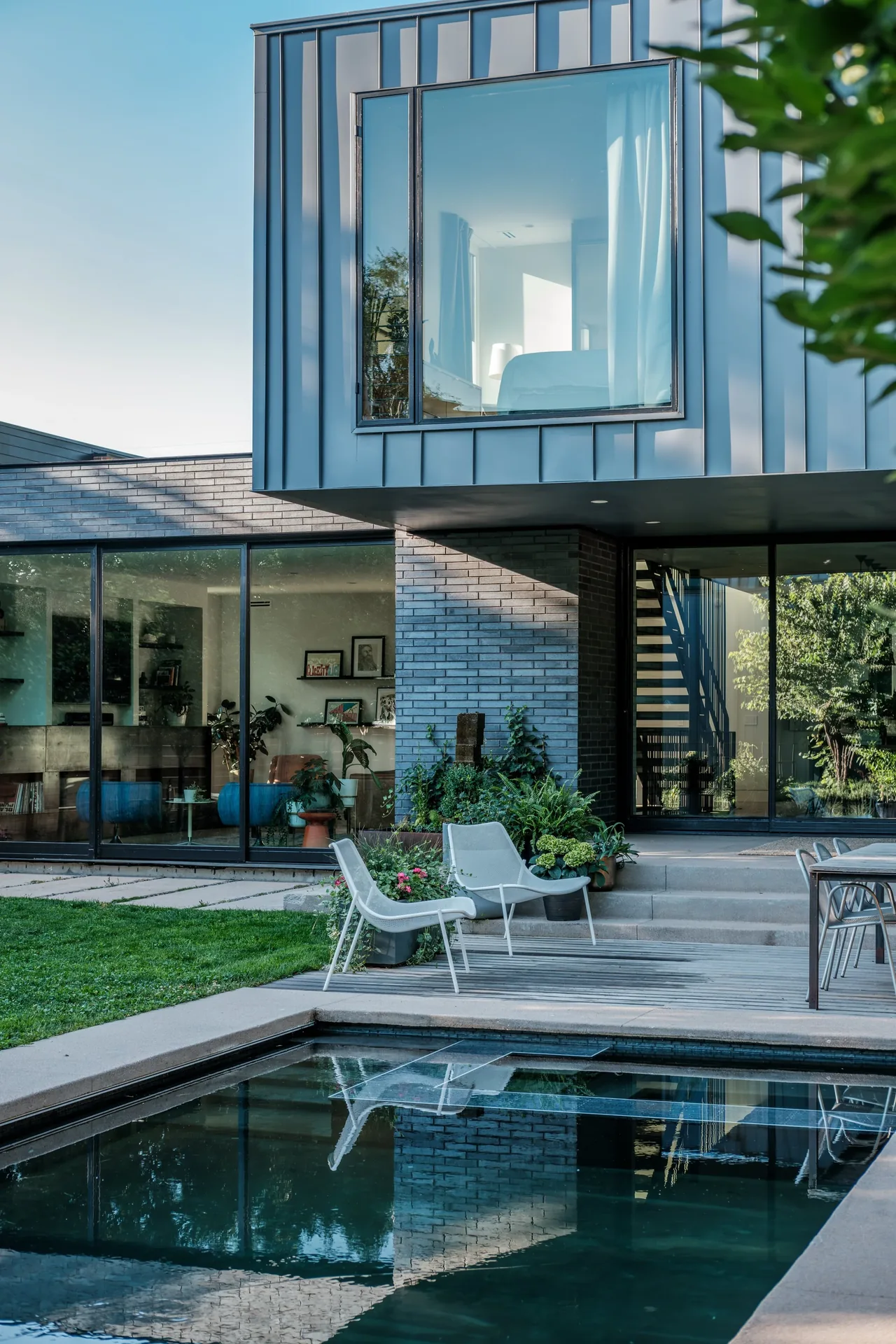 THE LOCUST HOME features vertical metal siding above dark brick facade and large floor-to-ceiling metal-framed windows.