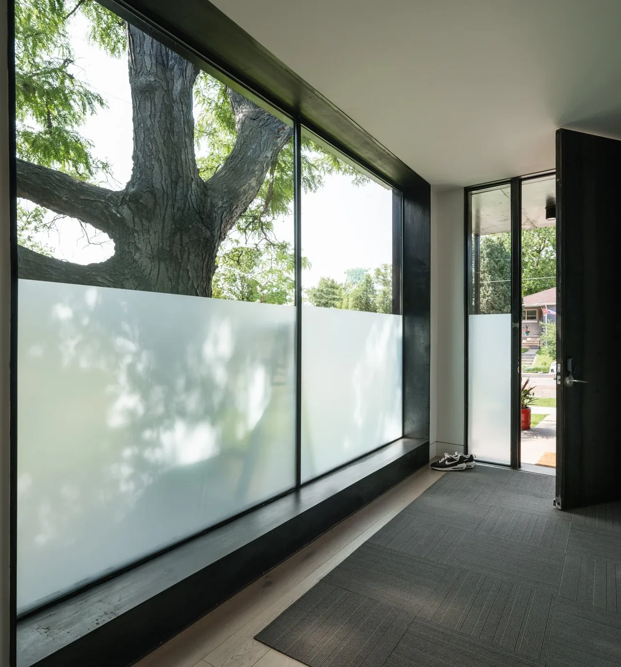 Entryway with floor-to-ceiling frosted glazing and black window frames at THE LOCUST HOME by DAVIS URBAN.