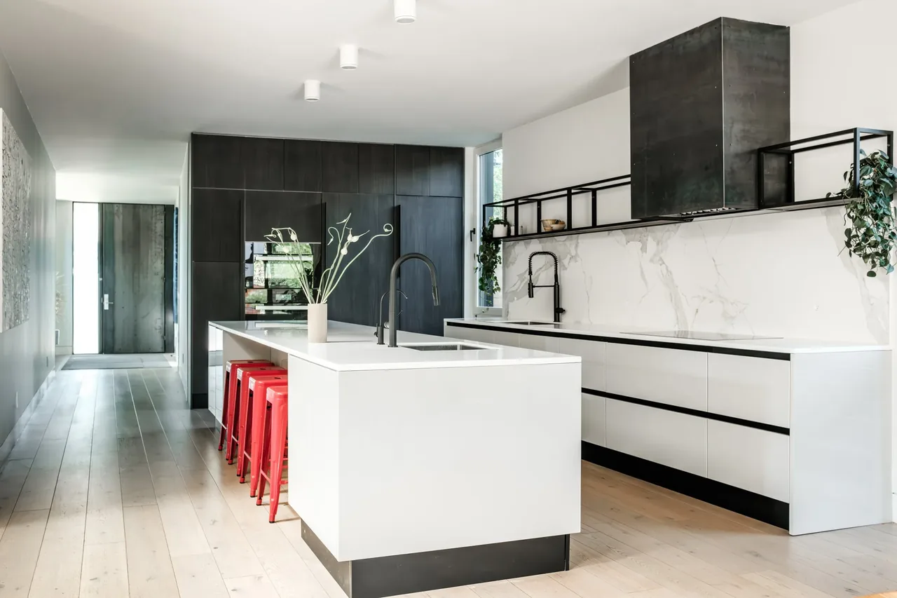 THE LOCUST HOME kitchen features a white island with red stools, dark cabinetry, and a black metal vent hood over the stove.