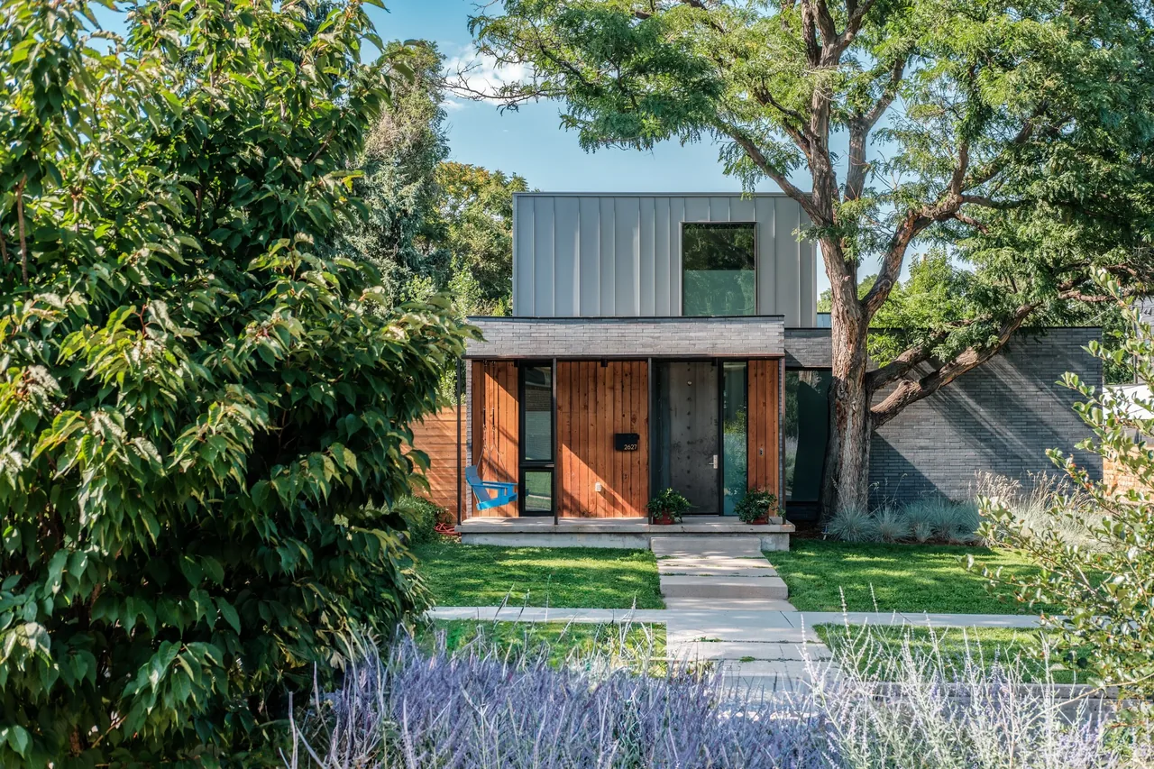 The Locust Home features a dark brick facade with a wooden porch and a mature tree near the concrete walkway.