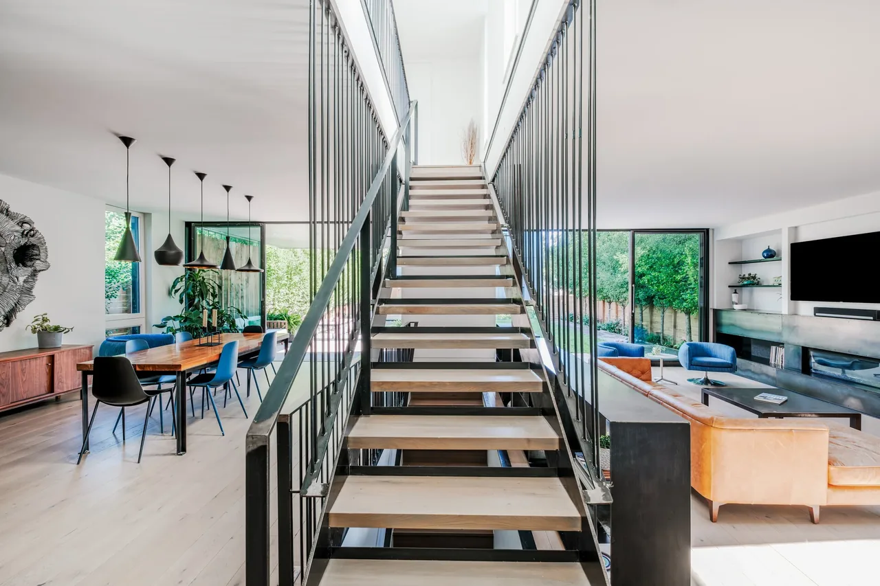 Open living and dining spaces separated by a modern floating staircase with black metal railings.