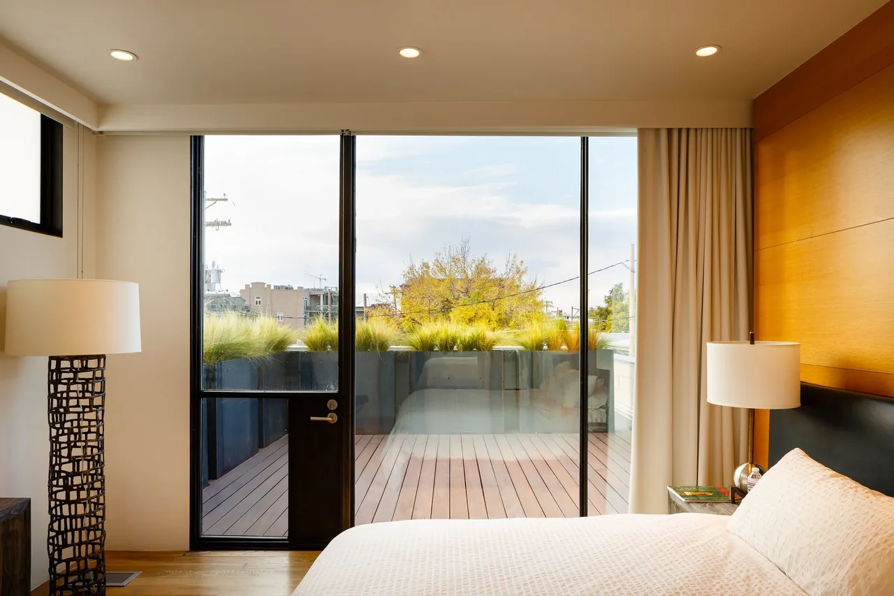 Bedroom with floor-to-ceiling black framed glass sliding doors leading to a balcony with plants.