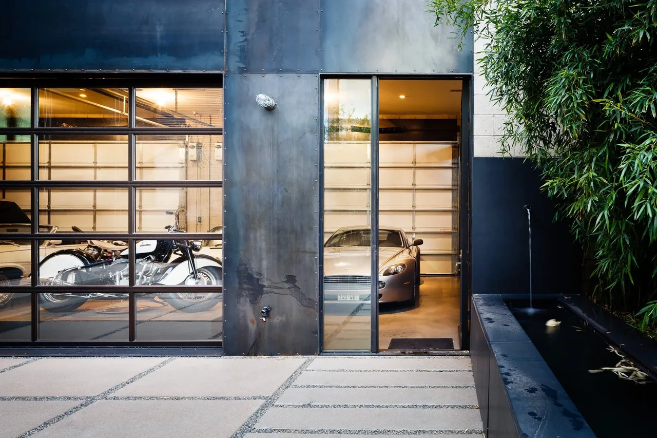 Garage with glass panel doors, black metal facade, and adjacent black water feature with bamboo plants.