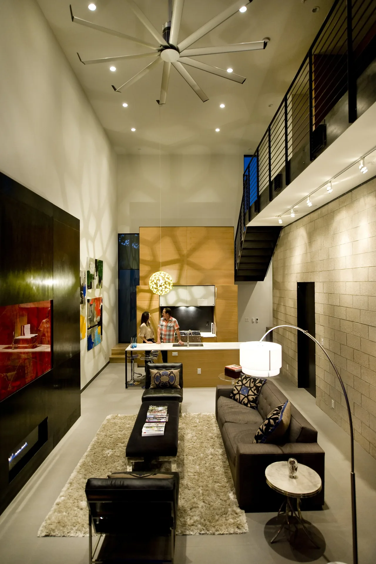 Modern living room with loft and minimalist kitchen showing high ceiling and concrete wall texture.