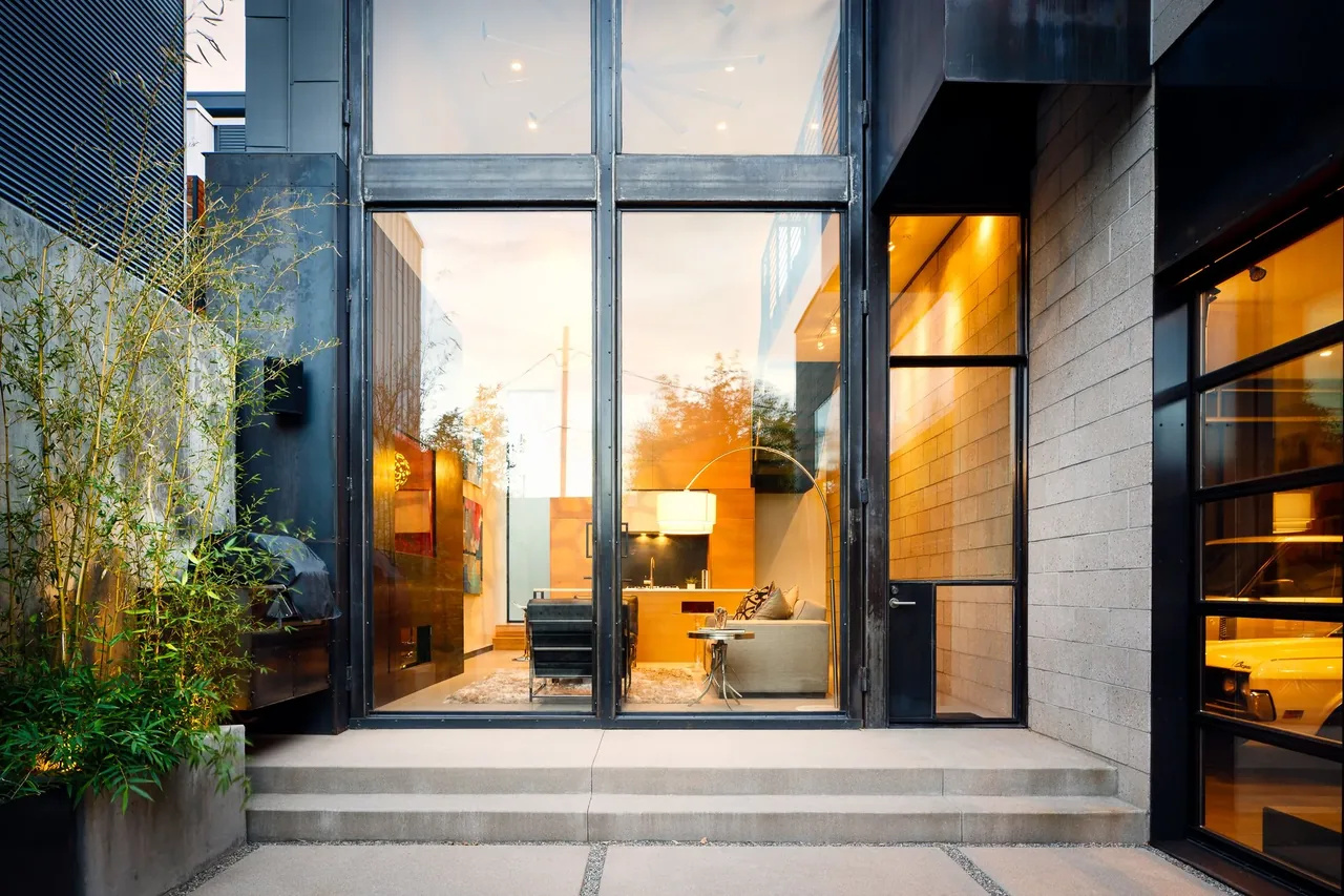 Modern living room visible through floor-to-ceiling glass with black steel framing and entrance door to the right.