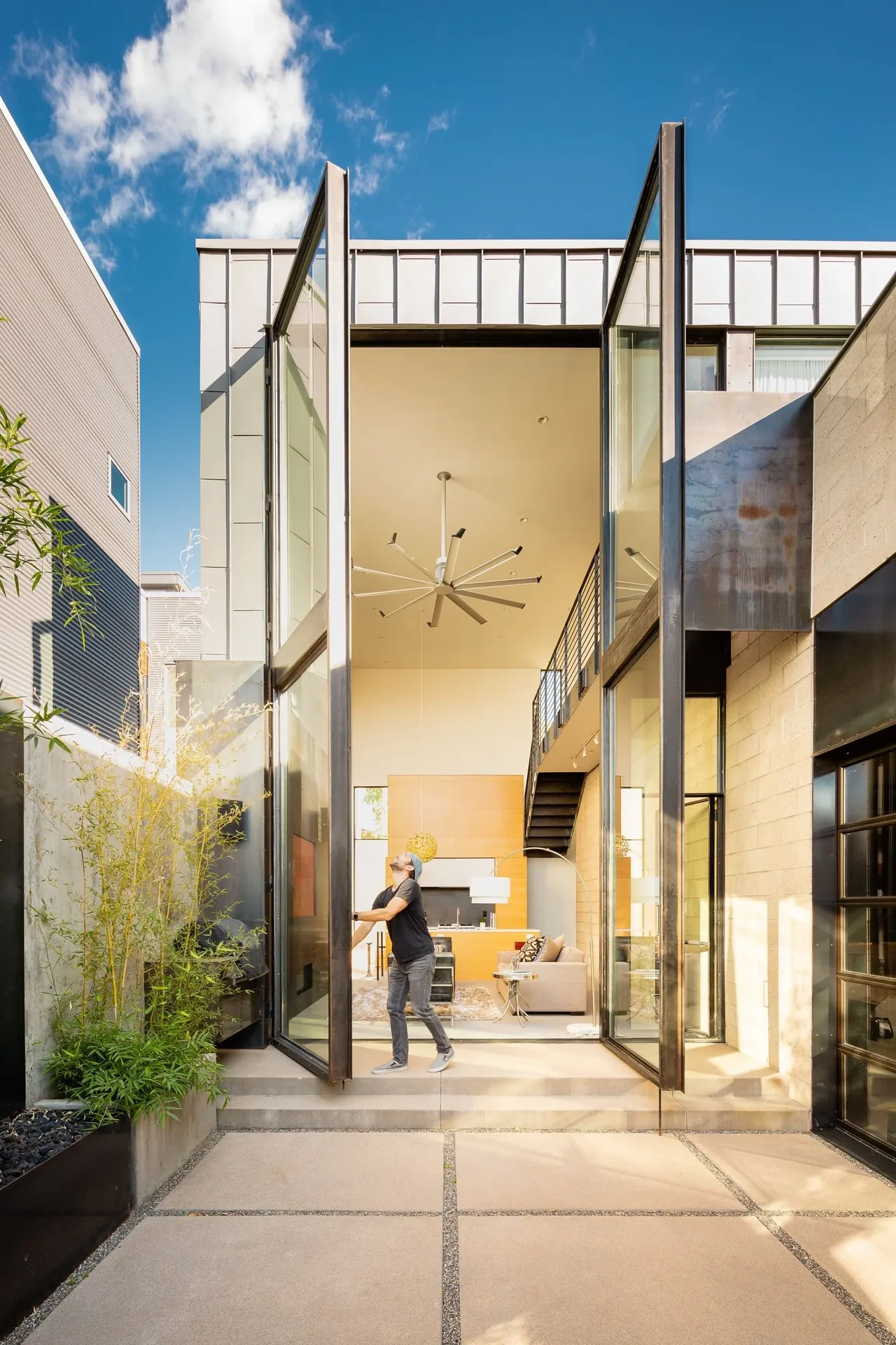 Tall folding glass doors open from patio into a modern living room with high ceiling and staircase.
