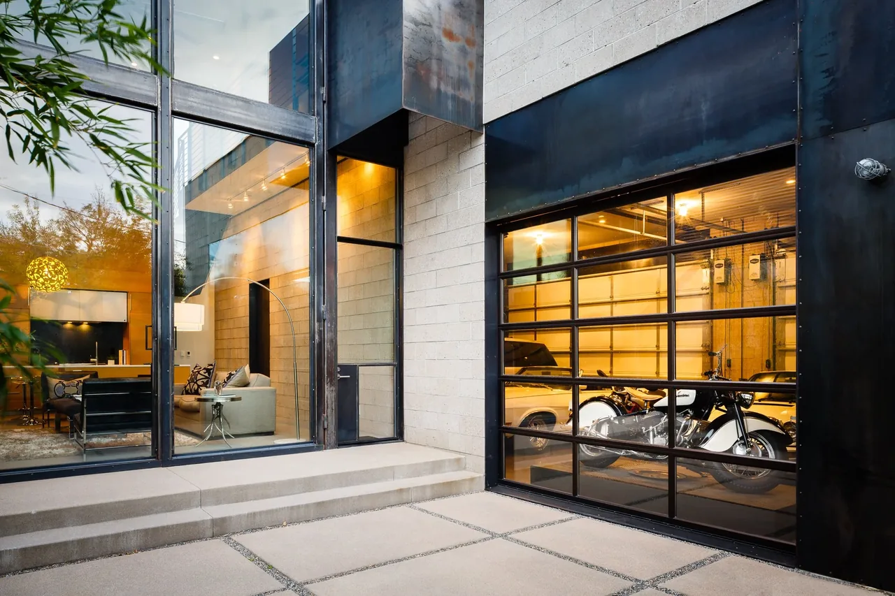 The alley house features a glass paneled garage door and adjacent full-height windows that illuminate the interior living space.