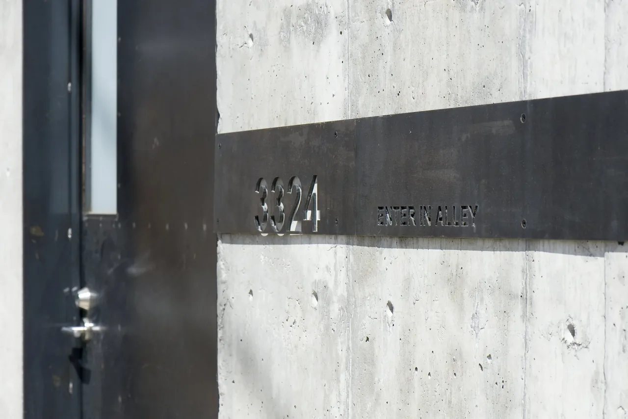 House number 3324 is cut out of a black metal plate mounted on a concrete wall, with an instruction to enter through the alley.