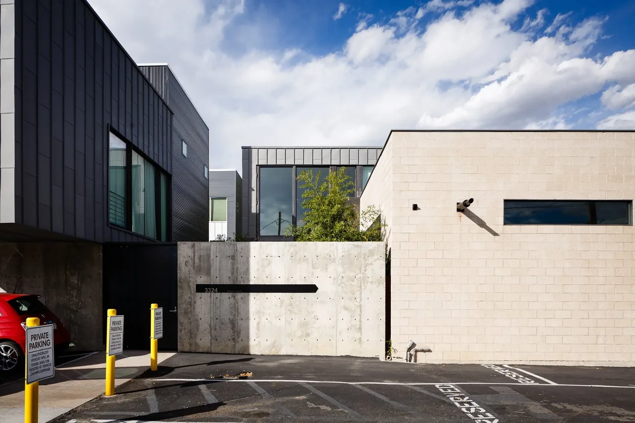 The alley house features a mix of concrete and beige brick facade with large black-framed windows and private parking spaces.