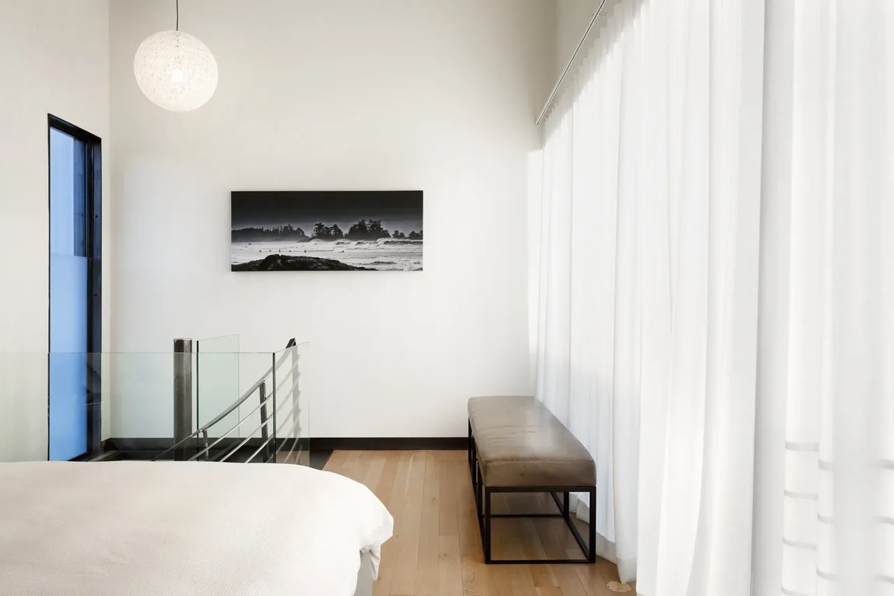 Bedroom corner with black metal framed bench and floor-to-ceiling white curtains in Alley House by DAVIS URBAN.