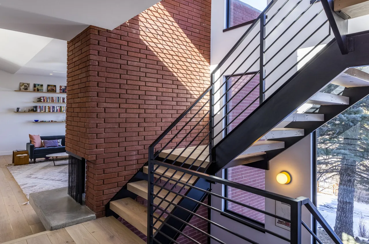 Interior view of a metal stair with wood treads alongside a floor-to-ceiling red brick fireplace wall.