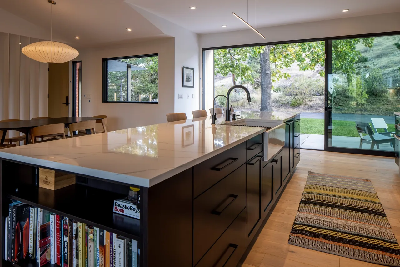 Kitchen interior featuring a large island with quartz countertop and black cabinetry overlooking a backyard with large sliding glass doors.