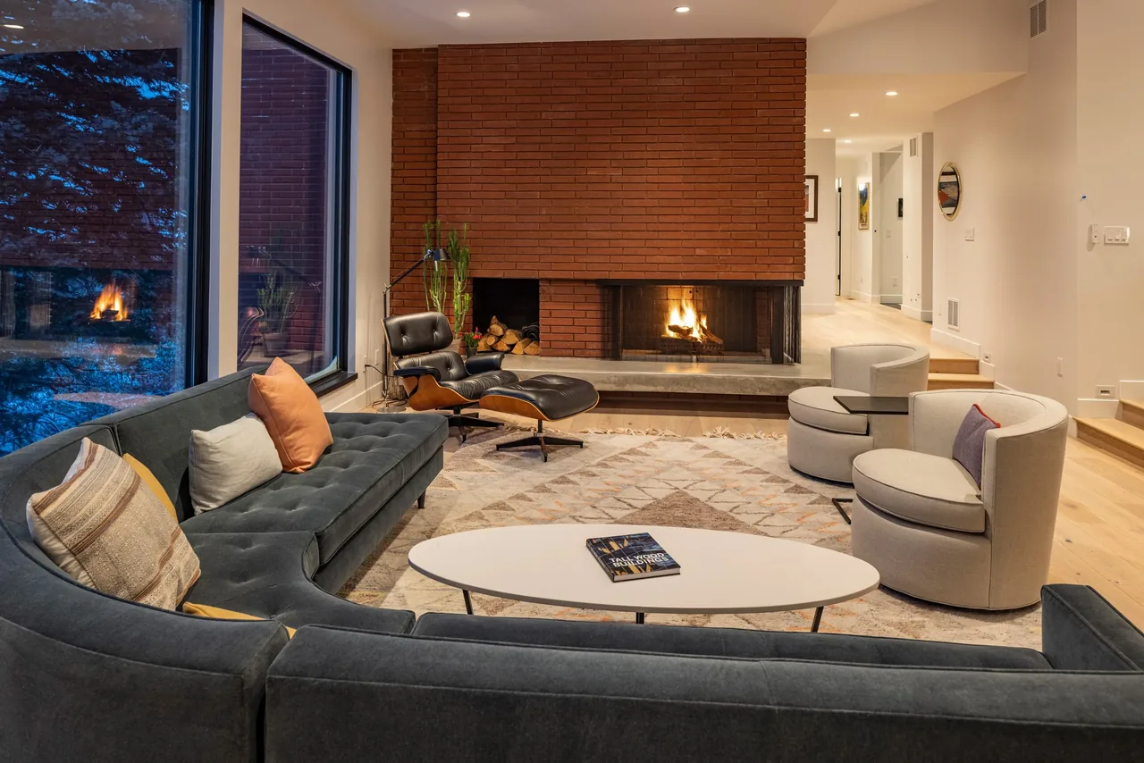 Living room featuring a brick fireplace, large sectional, and curved armchairs with a geometric rug on light wood flooring.