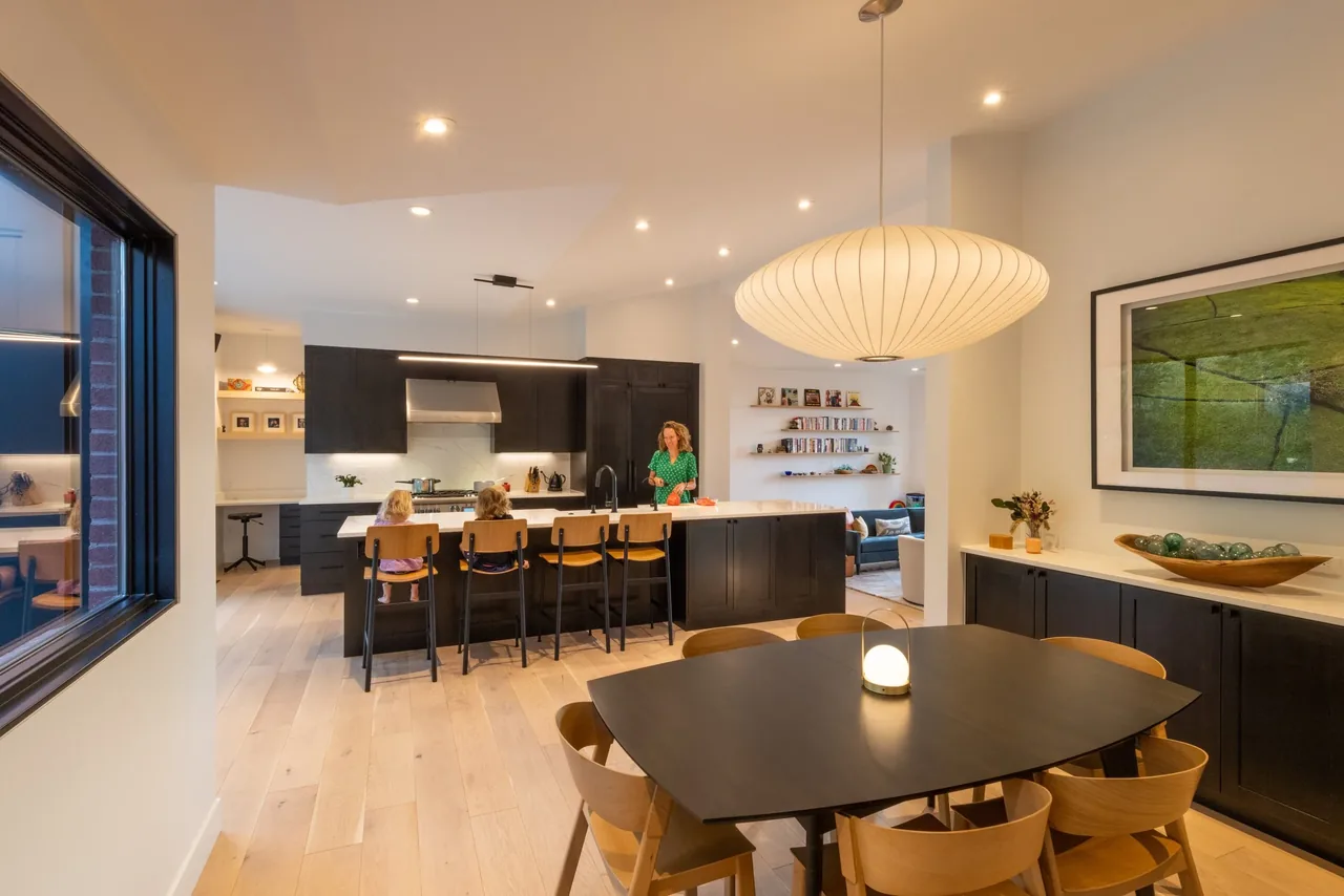 Open kitchen and dining area with black cabinets, wood flooring, and a large round pendant light.
