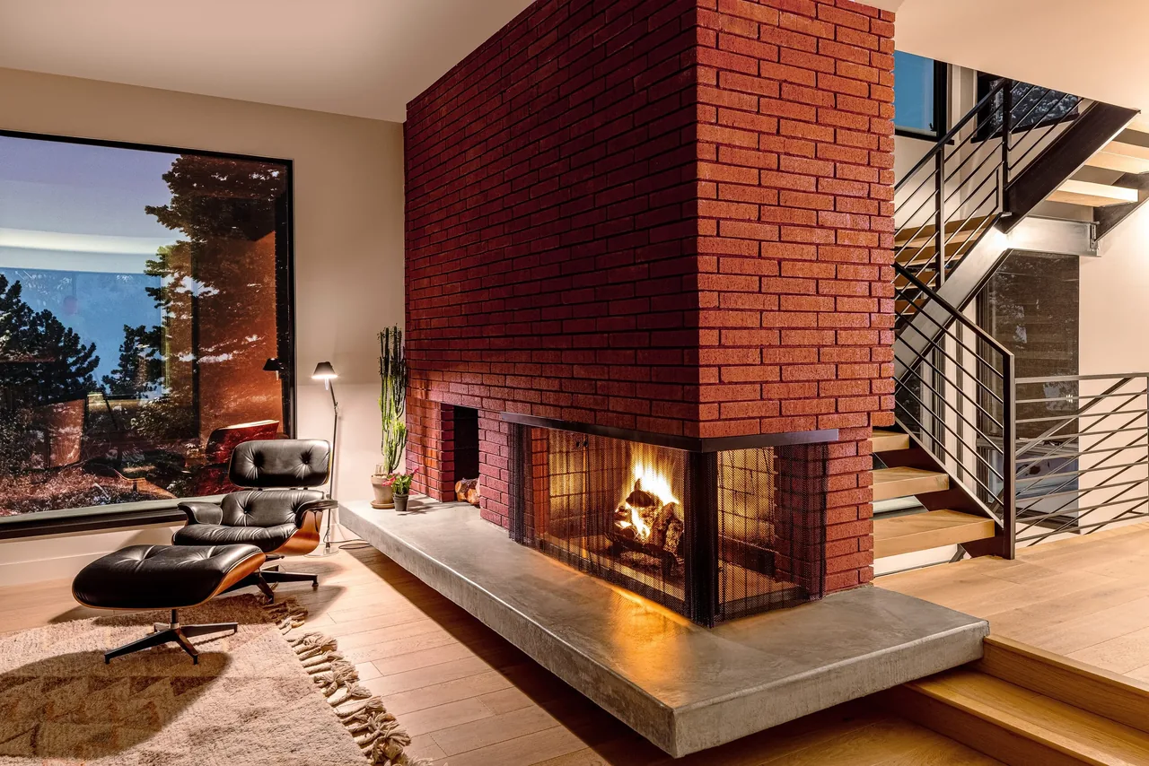 Living room with a double-sided red brick fireplace, modern metal-railing staircase, and wood flooring at the foothill project.