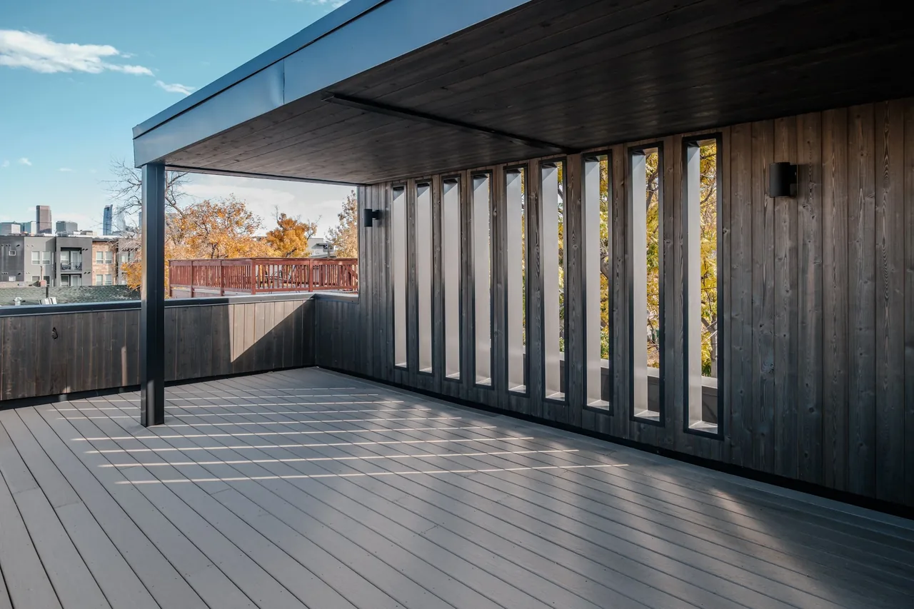 This outdoor patio features vertical rectangular windows and a dark wood ceiling with matching siding and a view of fall foliage.