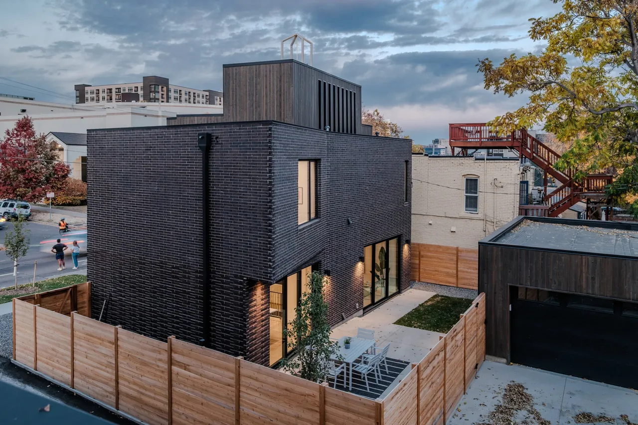 Street view of a two-story home featuring dark brick and vertical wood siding with a fenced outdoor patio and detached garage.