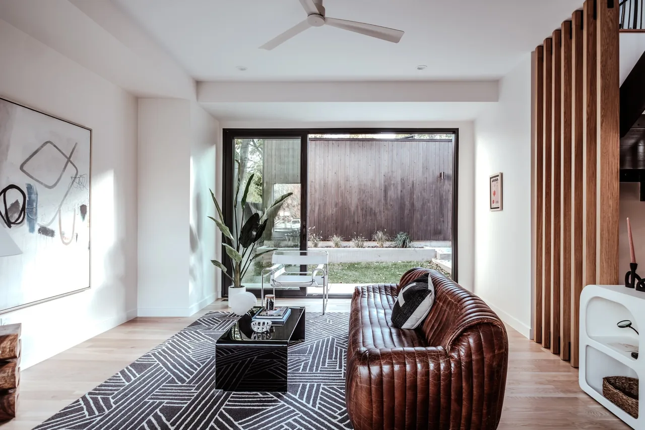 Living room features a brown leather sofa, geometric rug, and sliding glass door to outdoor fenced patio.