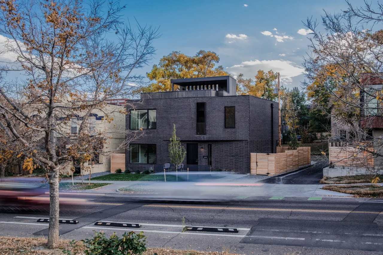 Modern black brick two-story residential building with prominent windows and a rooftop deck on a corner lot.