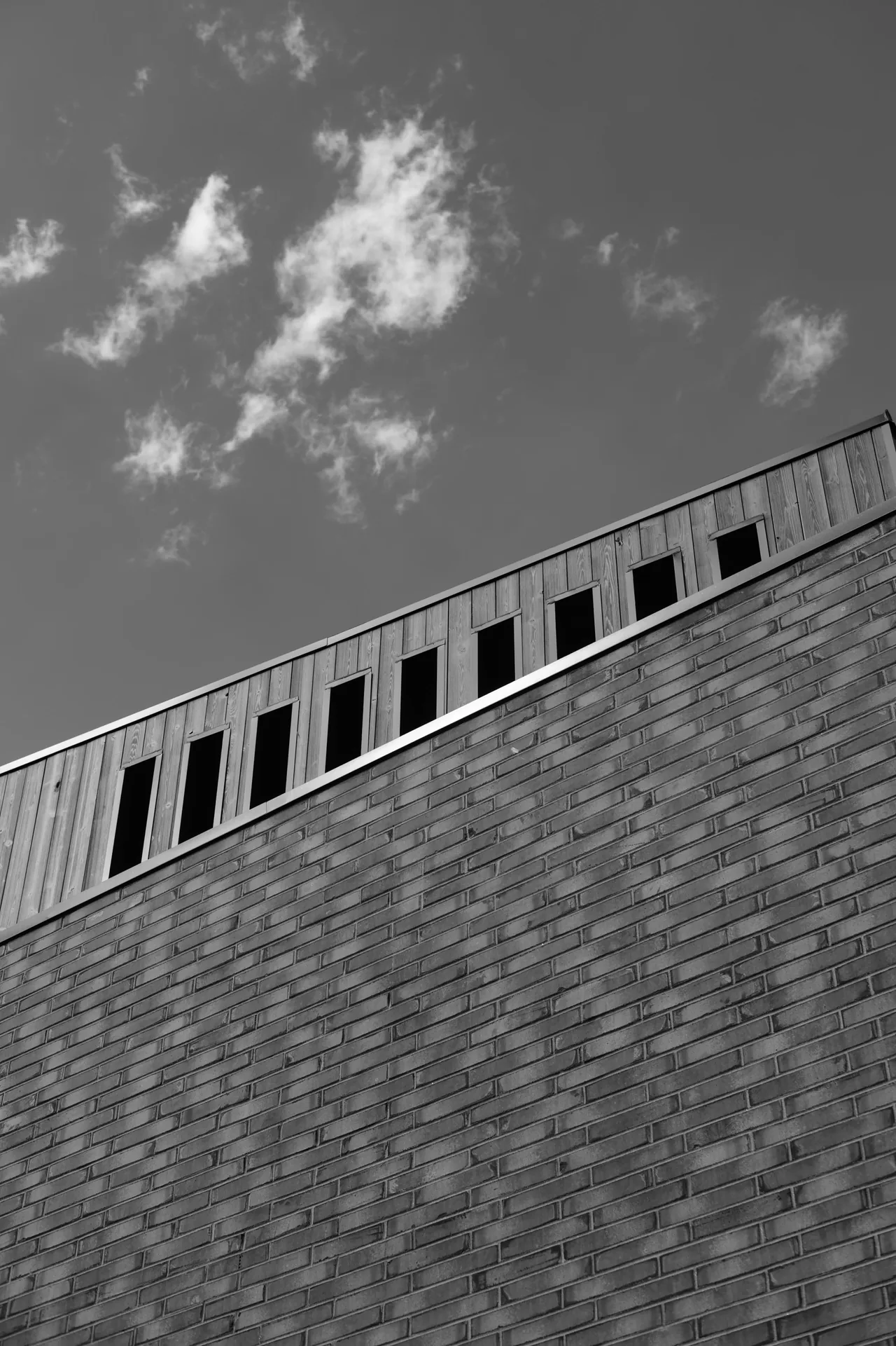 Brick wall with wood paneling and a row of small rectangular windows near the roofline.