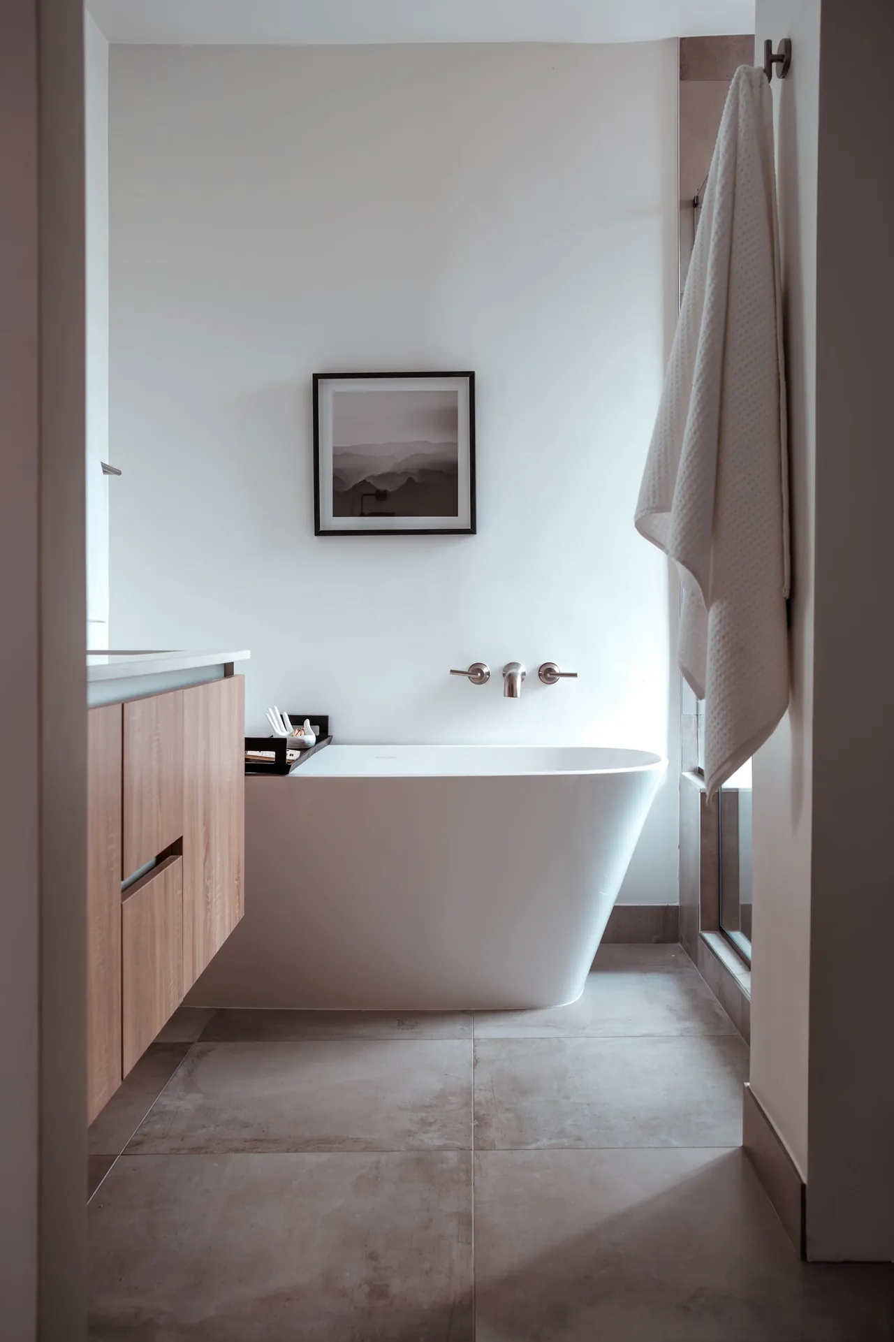 Minimalist bathroom with a freestanding tub, wall-mounted faucet, and wooden vanity.