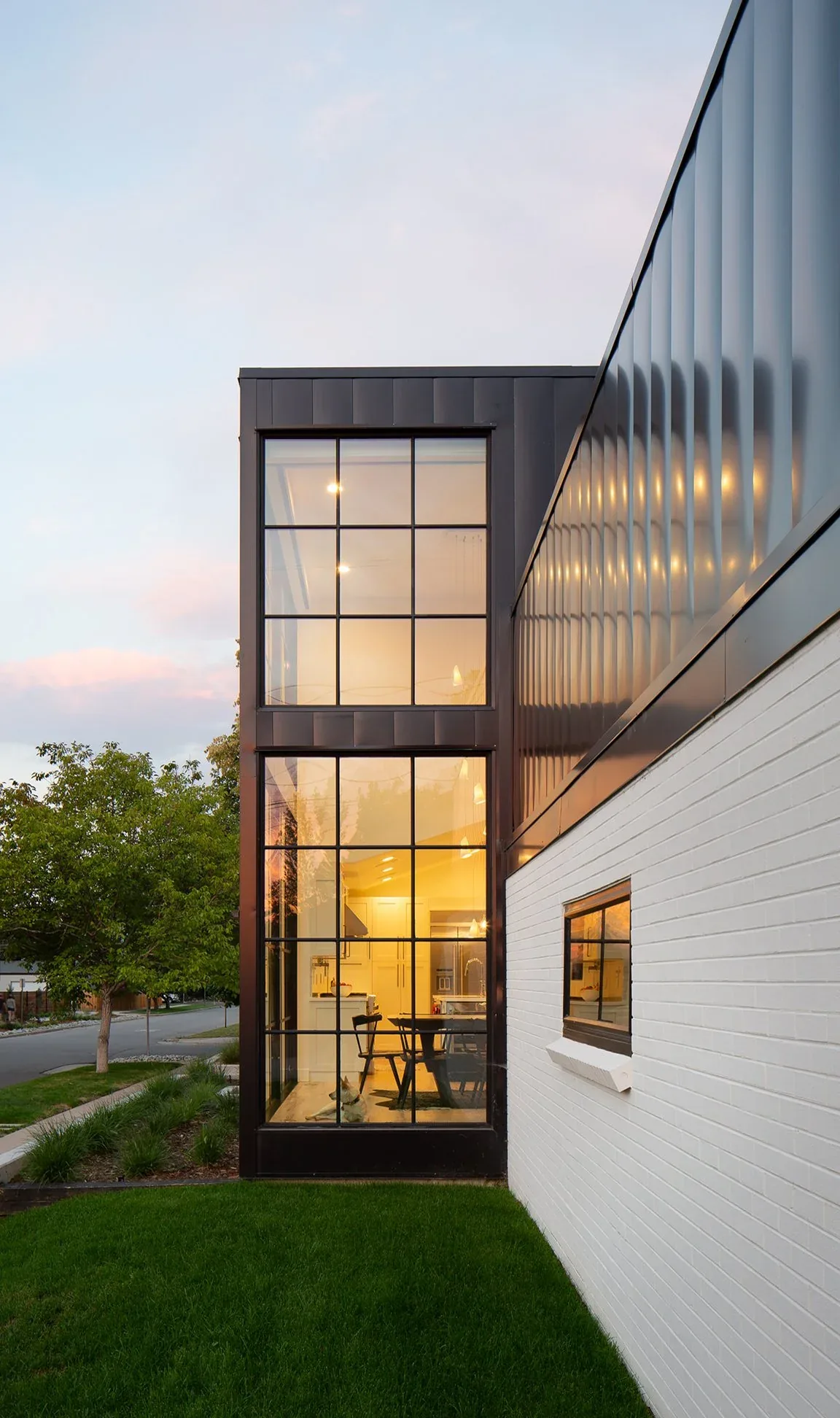 Black and White House exterior showcases large vertical grid windows and black metal siding above white brick walls.