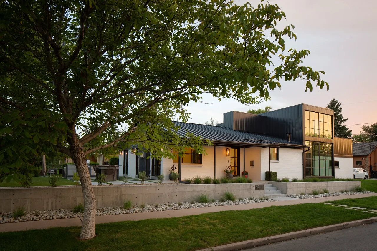 The Black and White House features a metal roof, vertical window grid, and a raised concrete planter by the front steps.